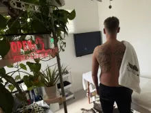 Client with tshirt off and angel wings back tattoo, with back to camera with a towel with my logo drapsed over shoulder